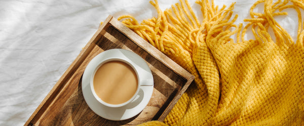 Coffee on a wood tray next to a yellow throw blanket