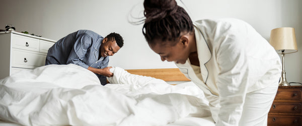 Couple putting sheets and comforter on bed