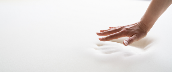 Hand pushing down on a memory foam mattress