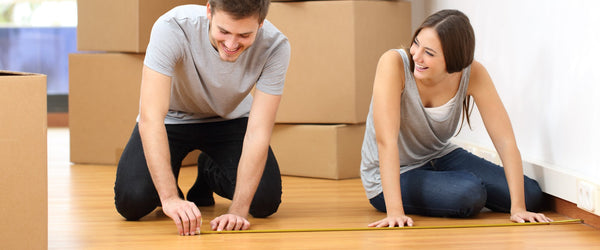 Couple measuring bedroom floor to decide on a bed size