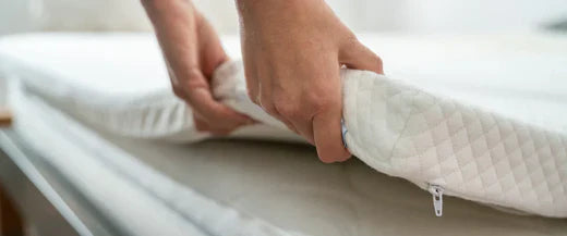 Hands placing a mattress topper on a mattress