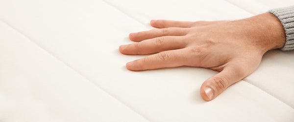 Hand pressing down on a mattress to test mattress firmness level